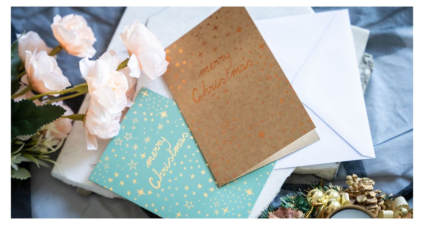 Two holiday cards with gold foil details surrounded by flowers and Christmas decoration, holiday card design inspiration.