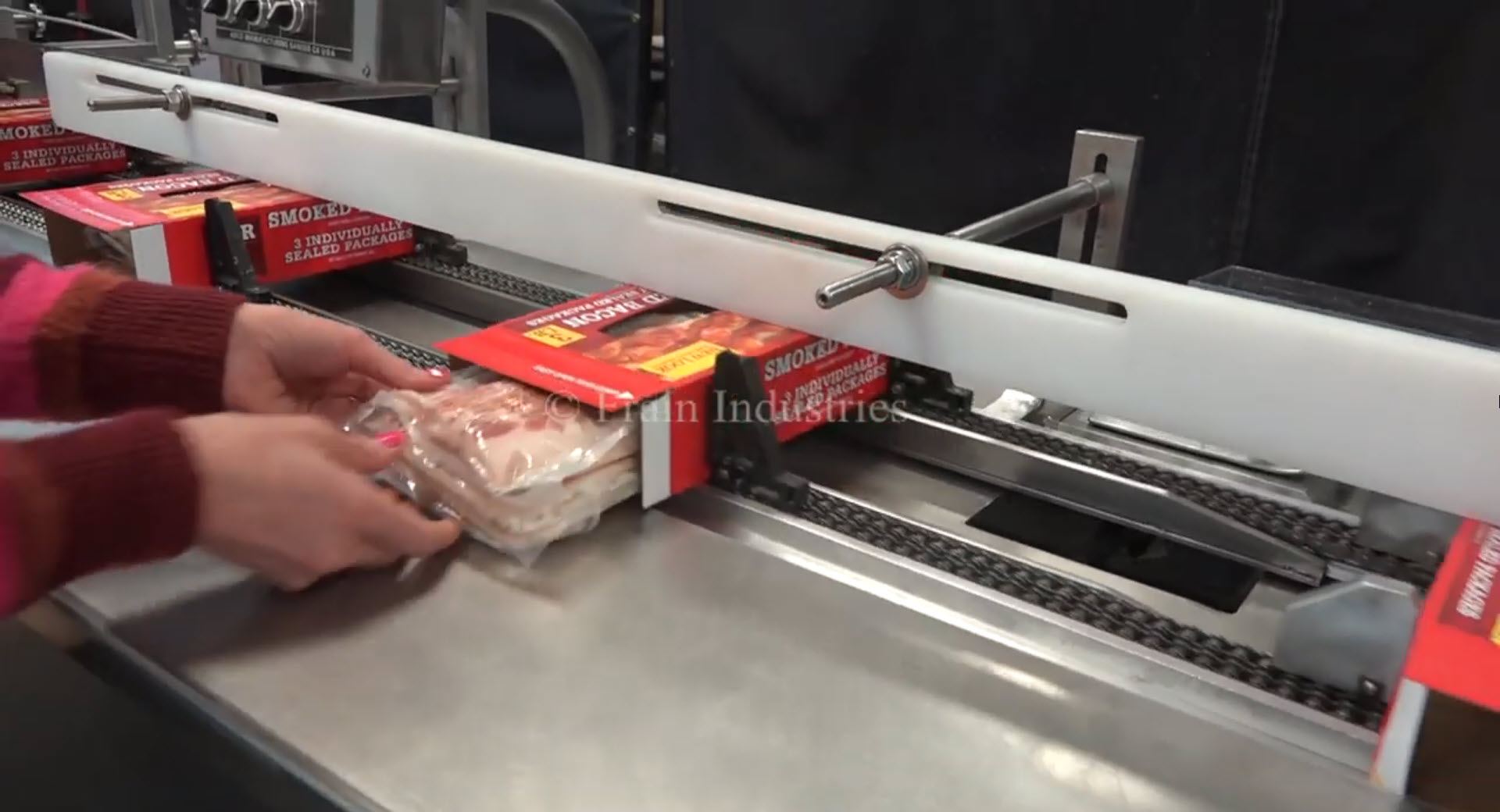Manual insertion of smoked bacon into a packaging box on a semi-automated cartoning machine.