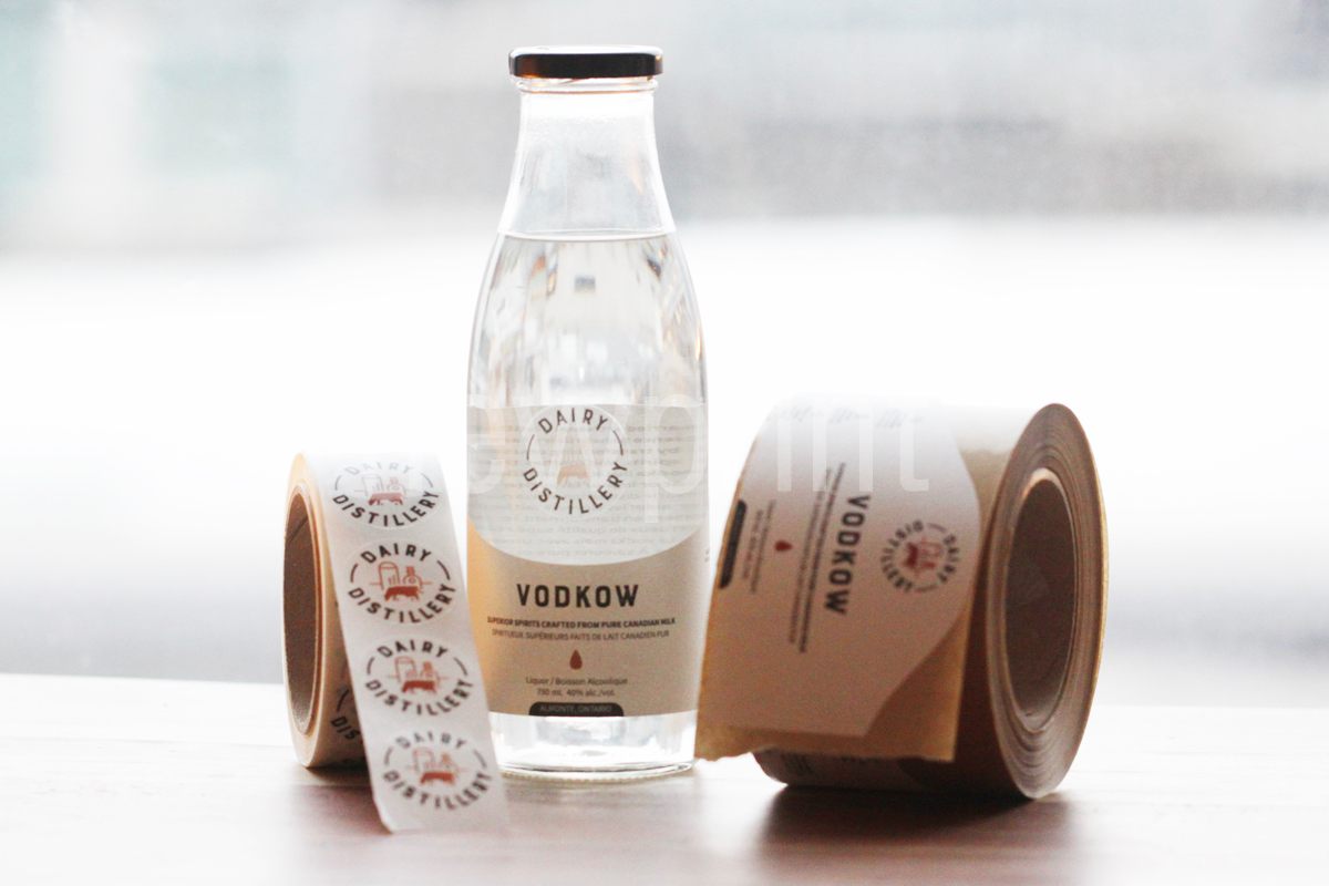 Guide to Custom Packaging-A glass bottle of spirit with two rolls of bottle labels on each side of the bottle.