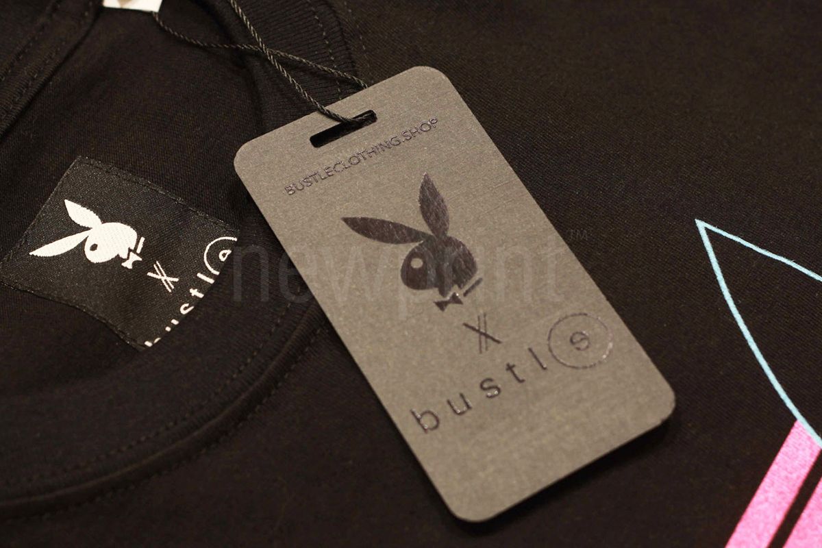 What is custom packaging - Gray t-shirt hang tag with silver foil details laying on top of a folded t-shirt.