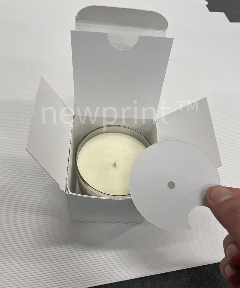 A blank prototype of a paperboard box with a candle inserted inside the box as a testing stage in the process of creating product packaging.