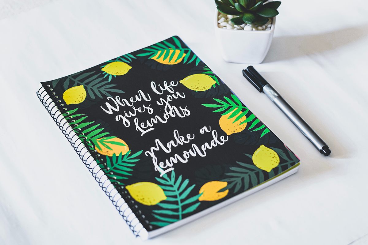 Wire bound planner on a white table and a pen next to the planner.