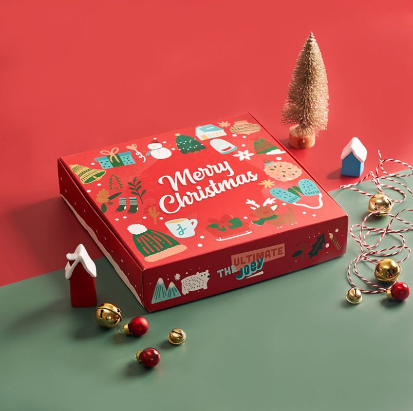 Red holiday packaging box with holiday ornaments around it.