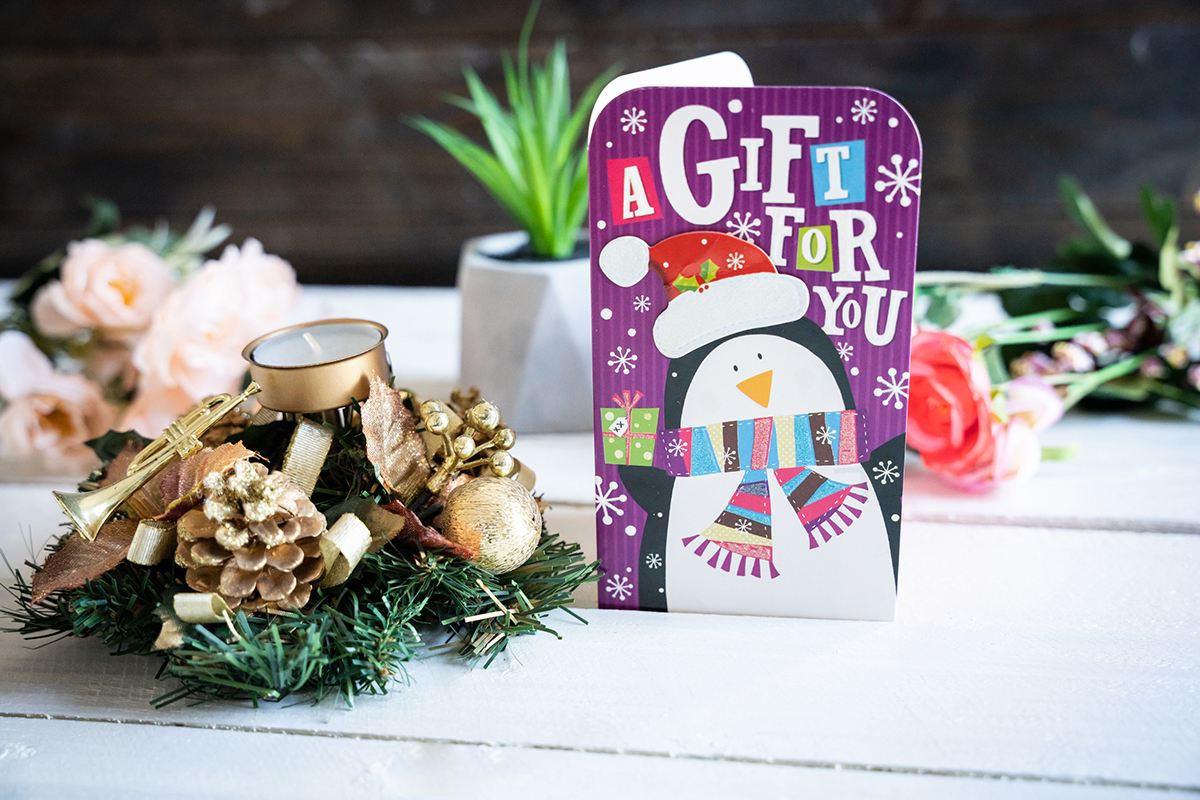 Holiday card on a white wooden background surrounded by christmas decorations and flowers.