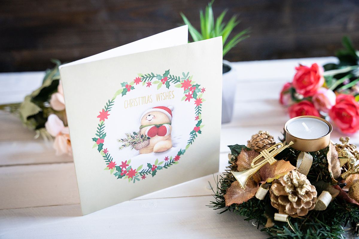 Folded holiday card on a white wooden background with christmas decorations around.