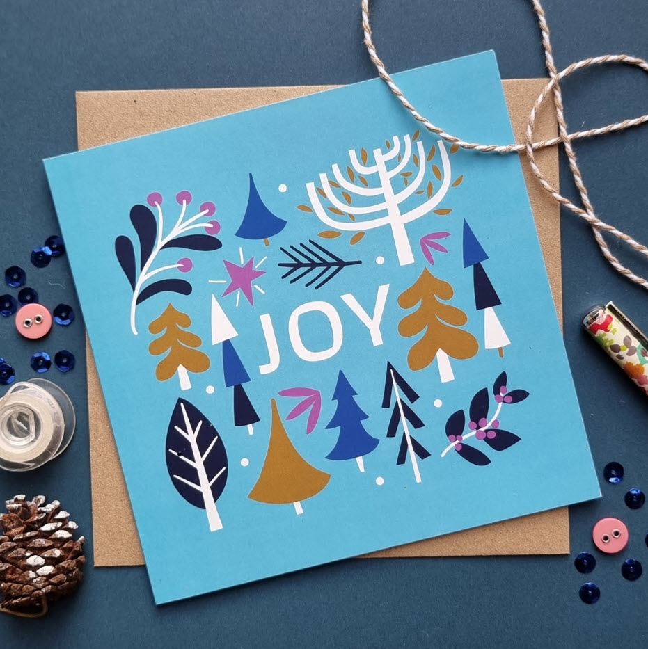 Holiday card on top of a kraft paper envelope with rope, buttons and a pencil around.