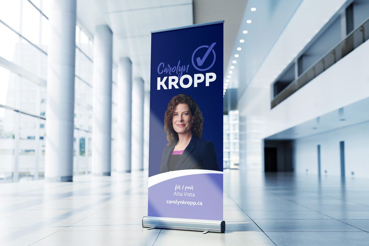 Roll banner promoting a municipal elections 2022 candidate inside a building hallway.