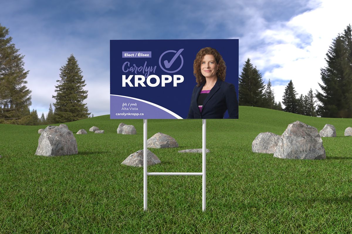 A yard sign promoting a municipal elections candidate placed on a grass field.