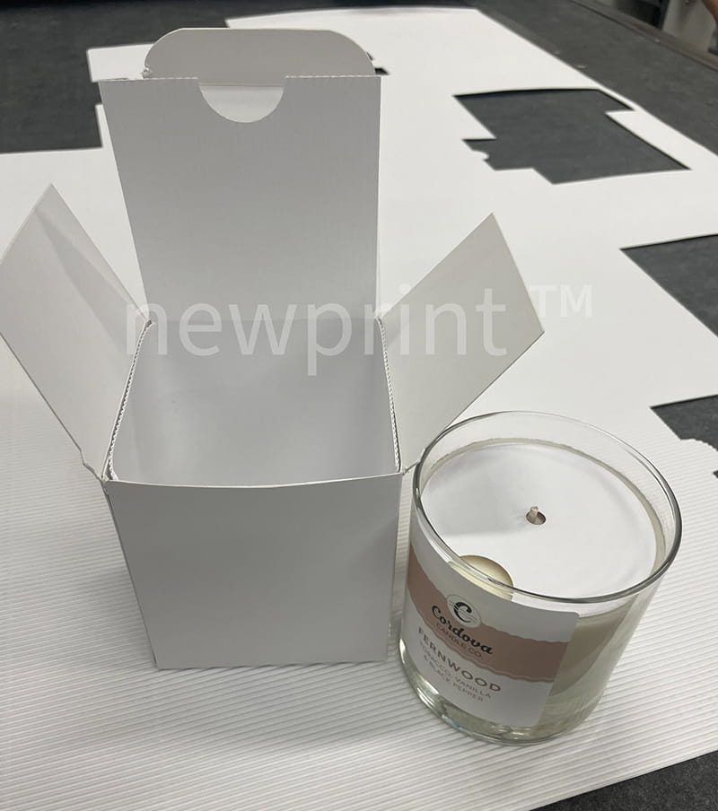 Open paperboard candle box. The candle with dust cover is next to it.