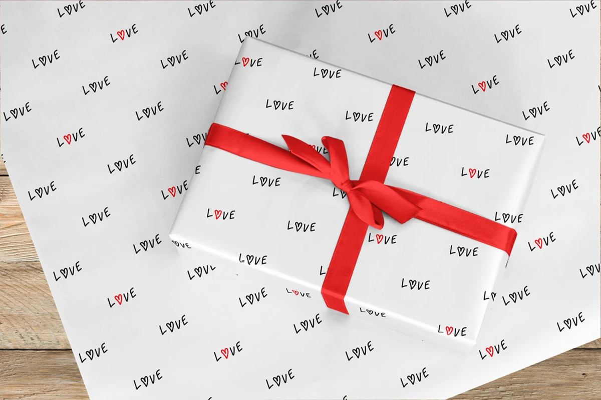 Packaged gift with simple wrapping paper with “love” written all around the white background.
