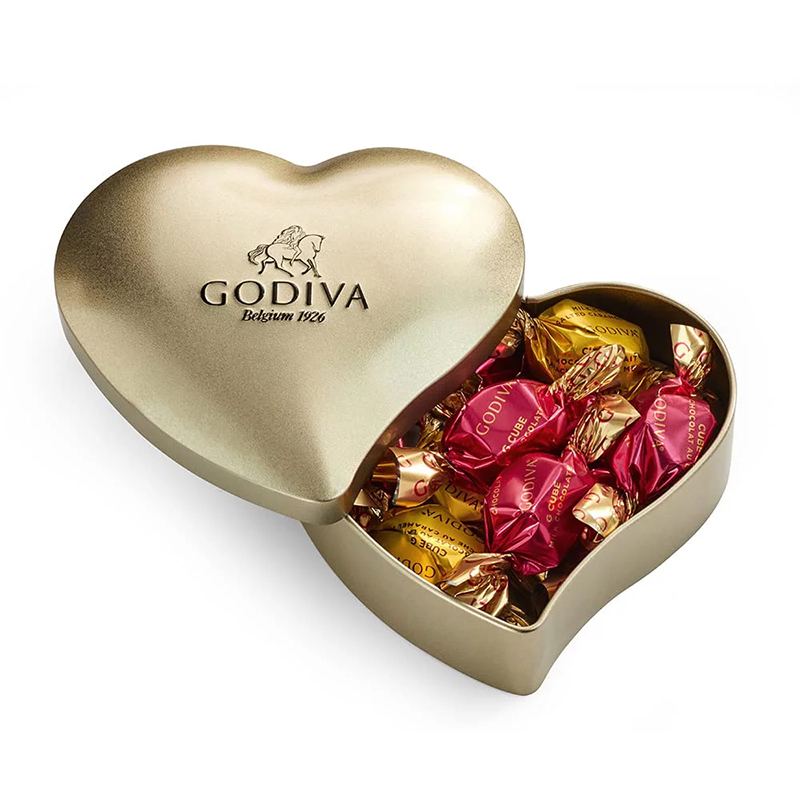 Valentine’s Day packaging, a light gold heart-shaped tin box with a base and a lid with the lid slightly opened showing various chocolates inside the box.